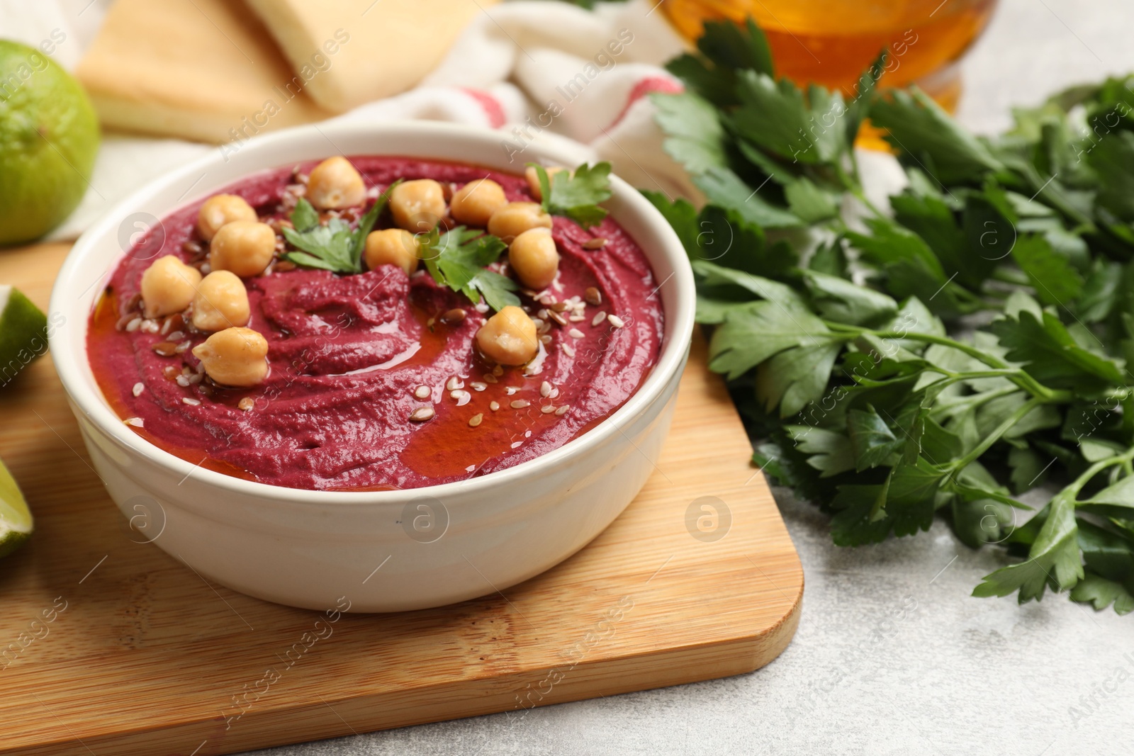 Photo of Tasty beet hummus with chickpeas and parsley in bowl on light table, closeup