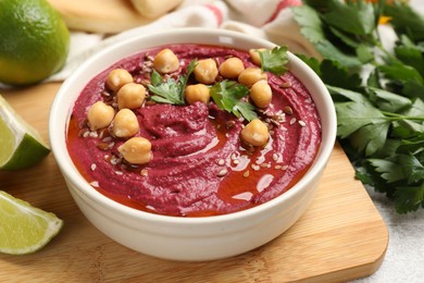 Photo of Tasty beet hummus with chickpeas and parsley in bowl on light table, closeup