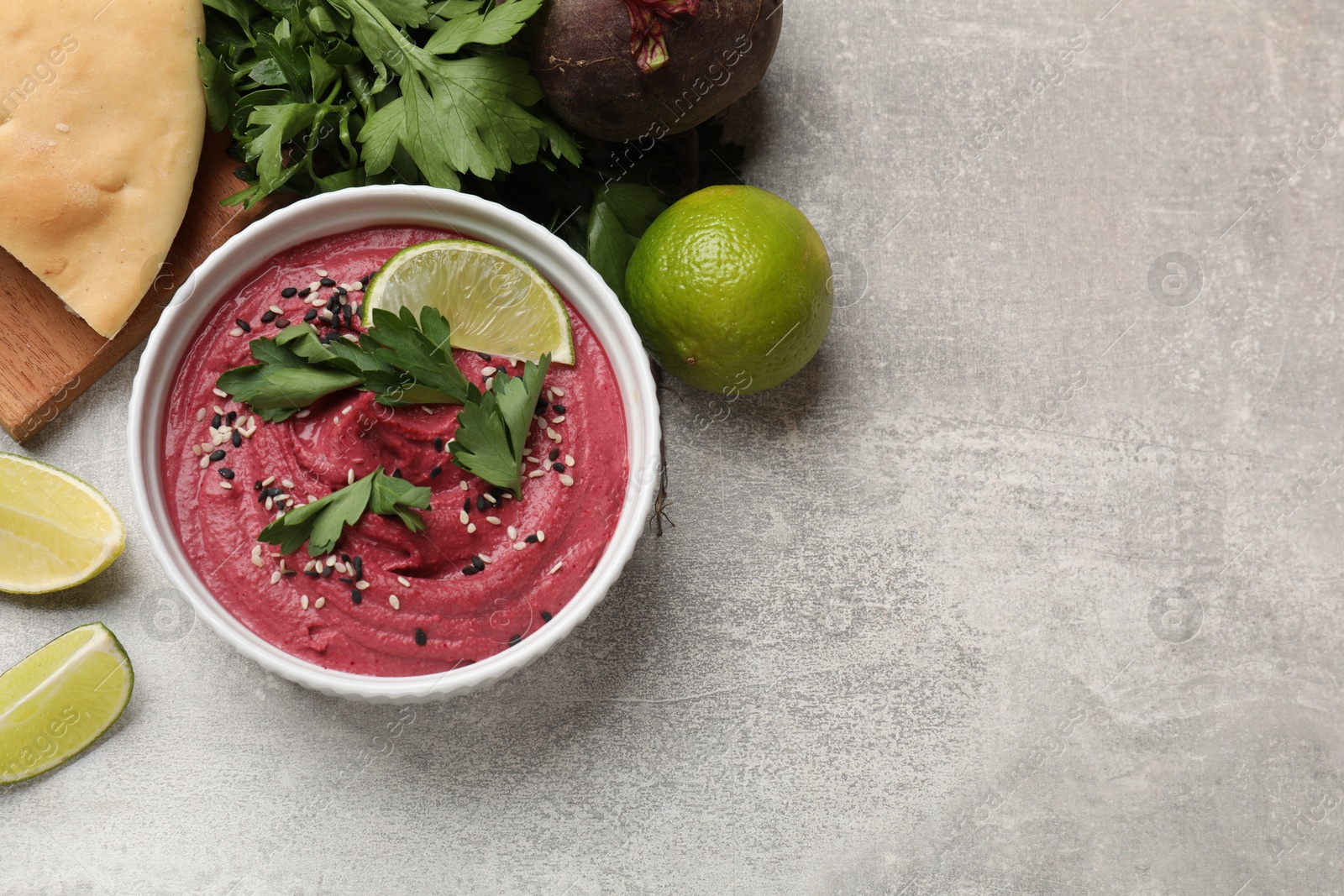 Photo of Tasty beet hummus with sesame and lime in bowl served on grey textured table, flat lay. Space for text