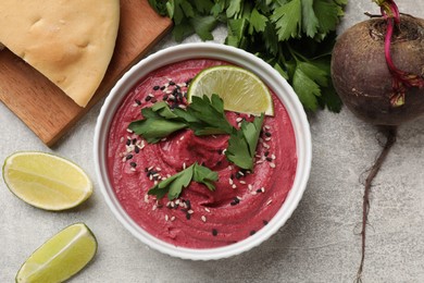 Photo of Tasty beet hummus with sesame in bowl served on grey textured table, flat lay