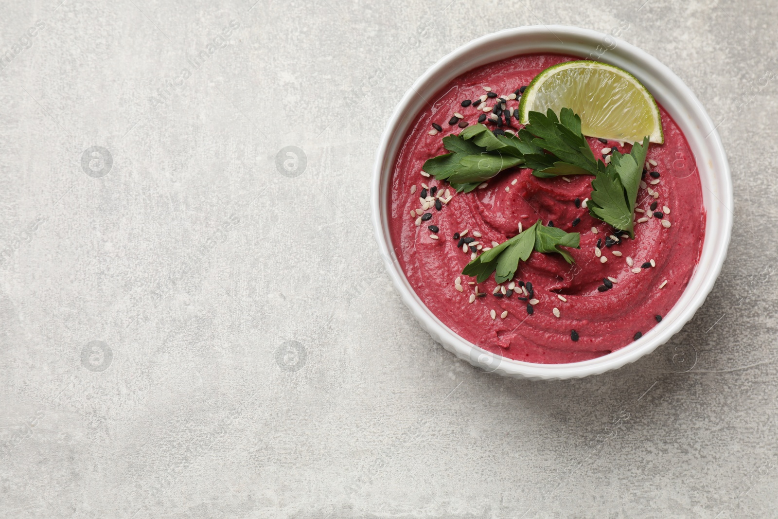 Photo of Tasty beet hummus with sesame and lime in bowl on grey textured table, top view. Space for text