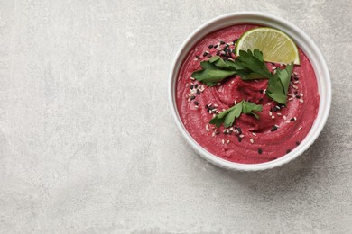 Photo of Tasty beet hummus with sesame and lime in bowl on grey textured table, top view. Space for text