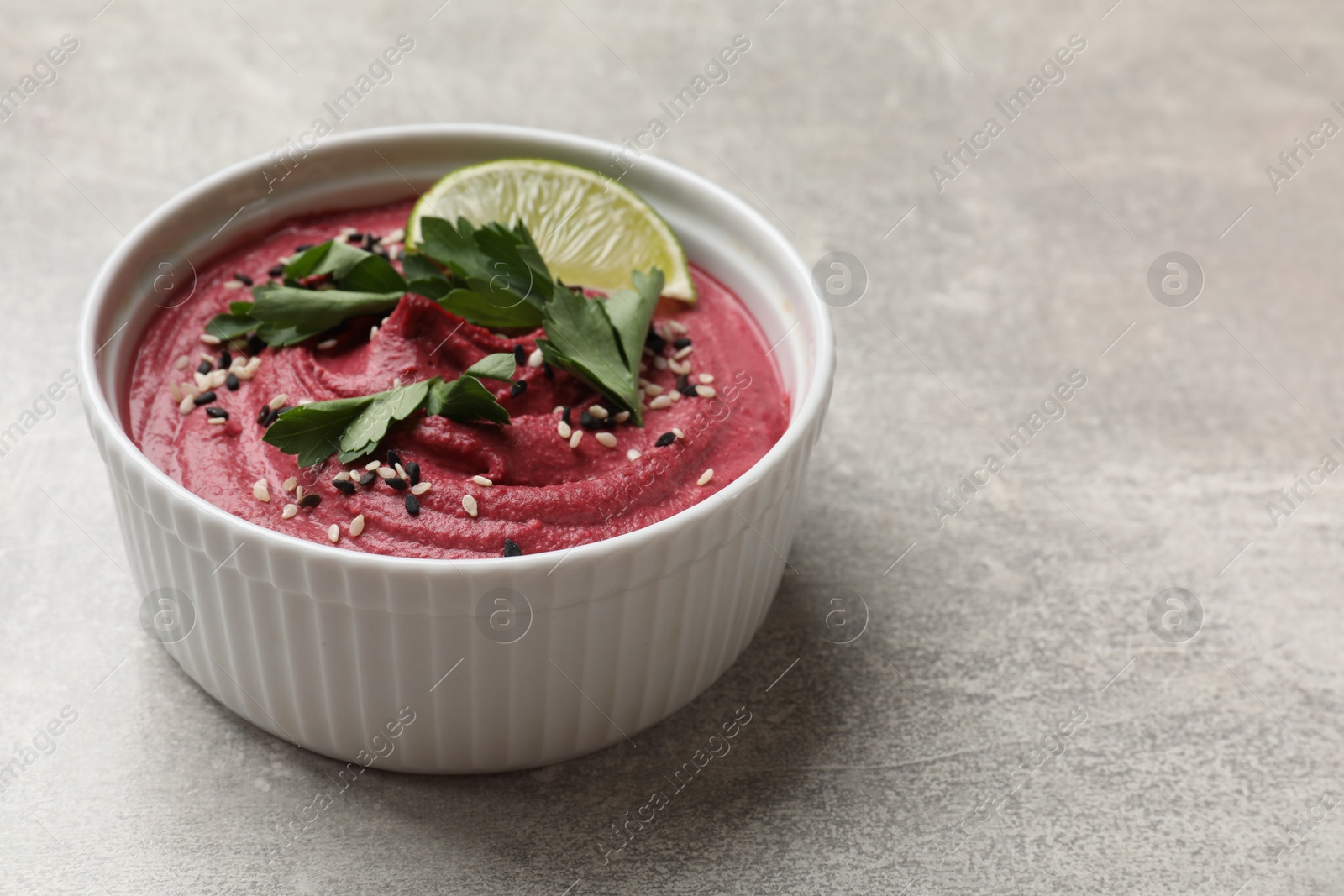 Photo of Tasty beet hummus with sesame and lime in bowl on grey textured table, closeup. Space for text