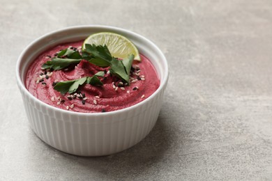 Photo of Tasty beet hummus with sesame and lime in bowl on grey textured table, closeup. Space for text