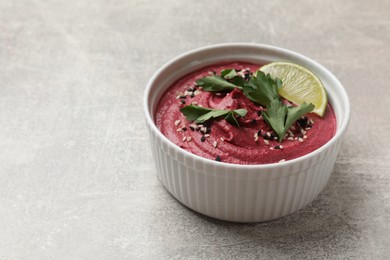 Photo of Tasty beet hummus with sesame and lime in bowl on grey textured table. Space for text