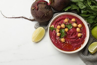 Photo of Tasty beet hummus with chickpeas in bowl and fresh ingredients on white table, flat lay. Space for text