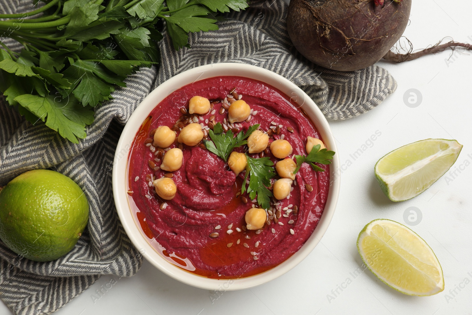 Photo of Tasty beet hummus with chickpeas in bowl and fresh ingredients on white table, flat lay