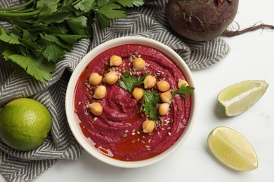 Tasty beet hummus with chickpeas in bowl and fresh ingredients on white table, flat lay