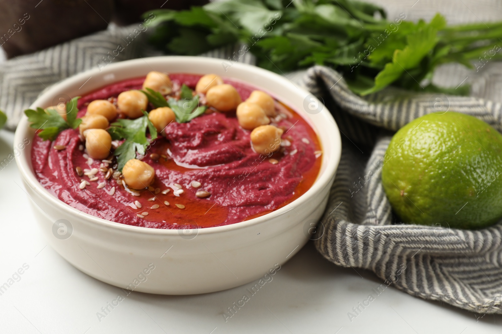 Photo of Tasty beet hummus with chickpeas and parsley in bowl on white table, closeup