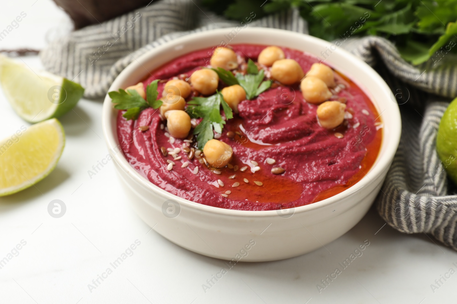 Photo of Tasty beet hummus with chickpeas and parsley in bowl on white table, closeup