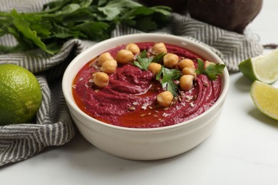 Photo of Tasty beet hummus with chickpeas and parsley in bowl on white table, closeup