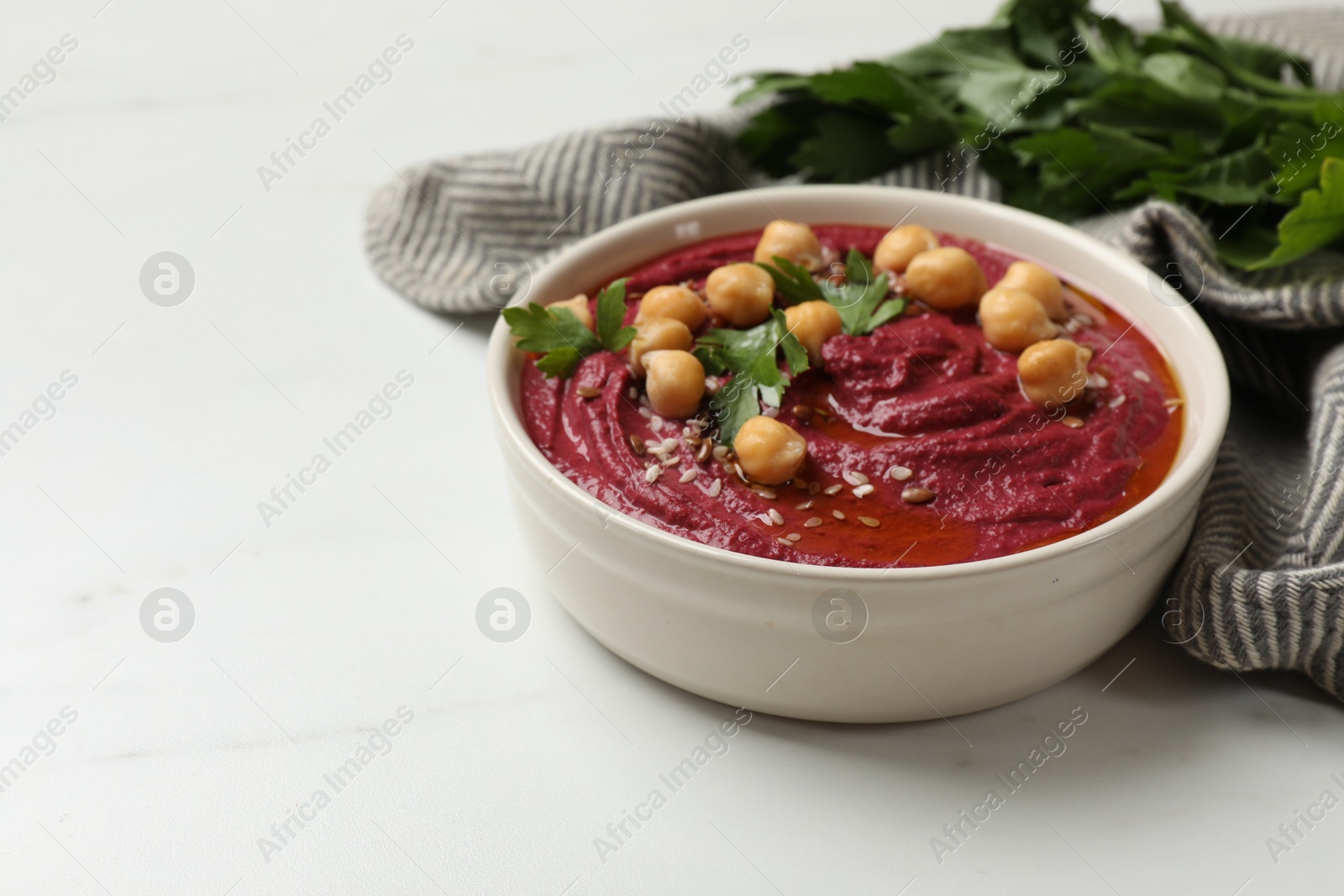 Photo of Tasty beet hummus with chickpeas and parsley in bowl on white marble table. Space for text