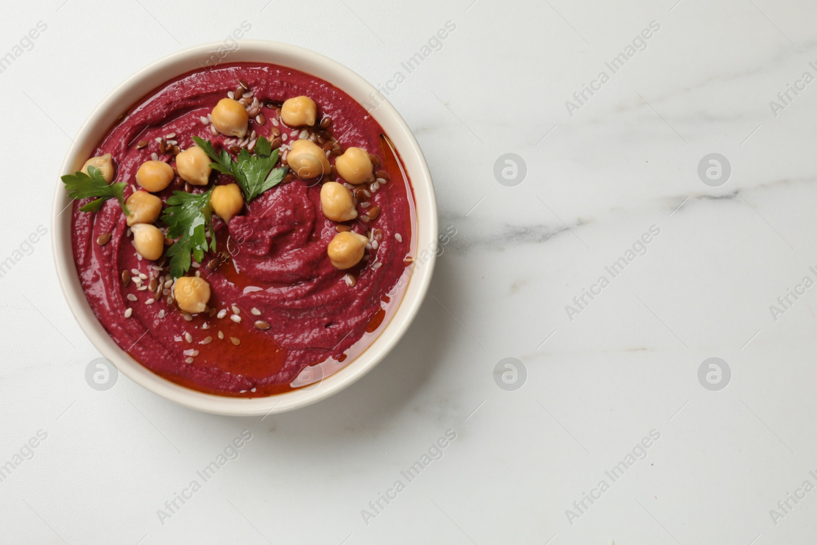 Photo of Tasty beet hummus with chickpeas and parsley in bowl on white marble table, top view. Space for text