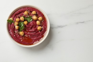 Tasty beet hummus with chickpeas and parsley in bowl on white marble table, top view. Space for text