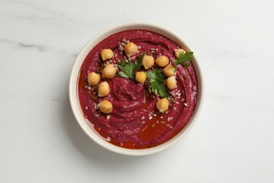 Tasty beet hummus with chickpeas and parsley in bowl on white marble table, top view