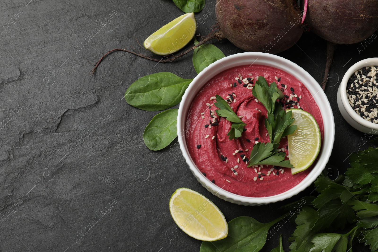 Photo of Tasty beet hummus in bowl and fresh ingredients on grey textured table, flat lay. Space for text