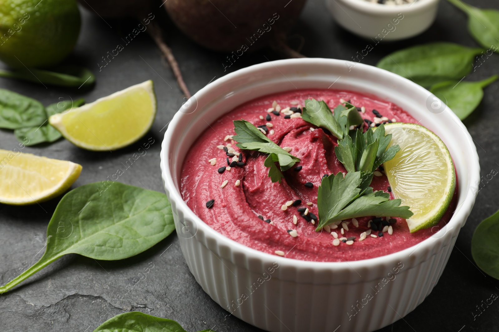 Photo of Tasty beet hummus with sesame and parsley in bowl on grey table, closeup