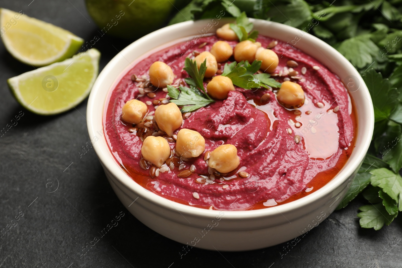 Photo of Tasty beet hummus with chickpeas and parsley in bowl on grey textured table, closeup