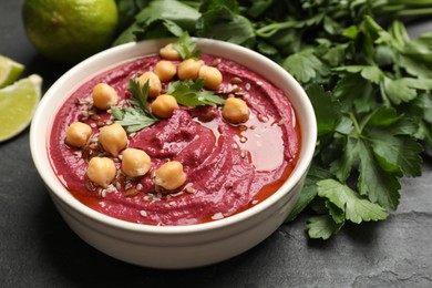 Photo of Tasty beet hummus with chickpeas and parsley in bowl on grey textured table, closeup