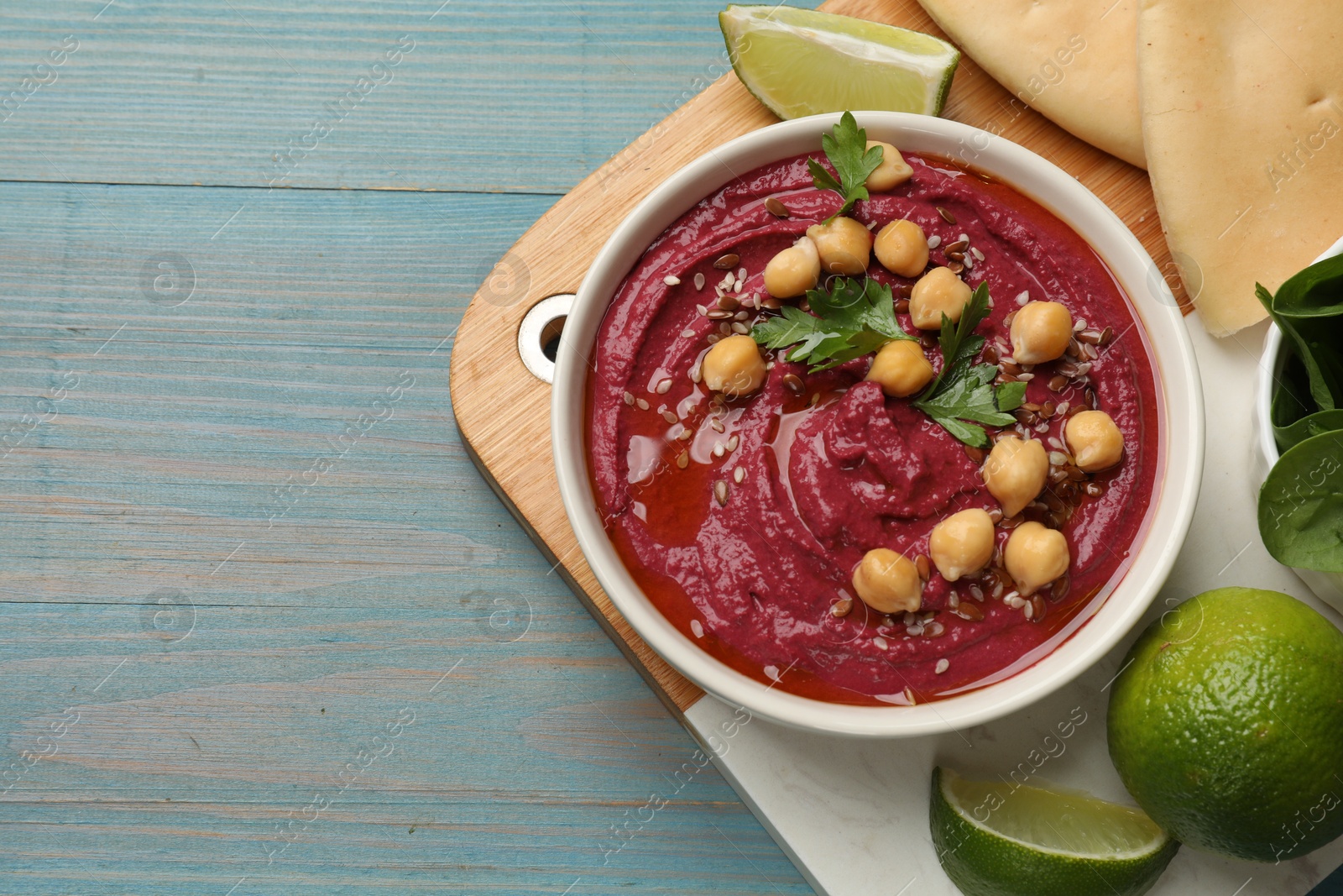 Photo of Tasty beet hummus with chickpeas in bowl served on light blue wooden table, flat lay. Space for text