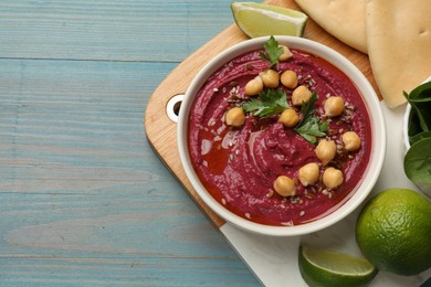 Photo of Tasty beet hummus with chickpeas in bowl served on light blue wooden table, flat lay. Space for text