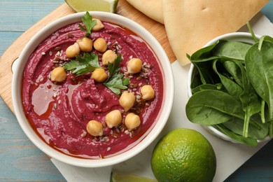 Photo of Tasty beet hummus with chickpeas in bowl served on light blue wooden table, flat lay