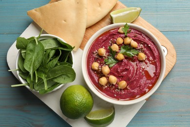 Photo of Tasty beet hummus with chickpeas in bowl served on light blue wooden table, flat lay