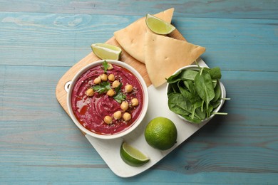 Photo of Tasty beet hummus with chickpeas in bowl served on light blue wooden table, flat lay