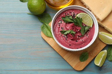 Photo of Tasty beet hummus with lime in bowl served on light blue wooden table, flat lay. Space for text