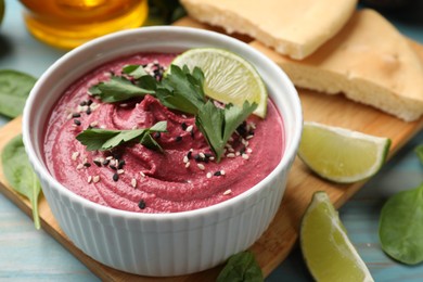 Photo of Tasty beet hummus with parsley and lime in bowl on light blue table, closeup