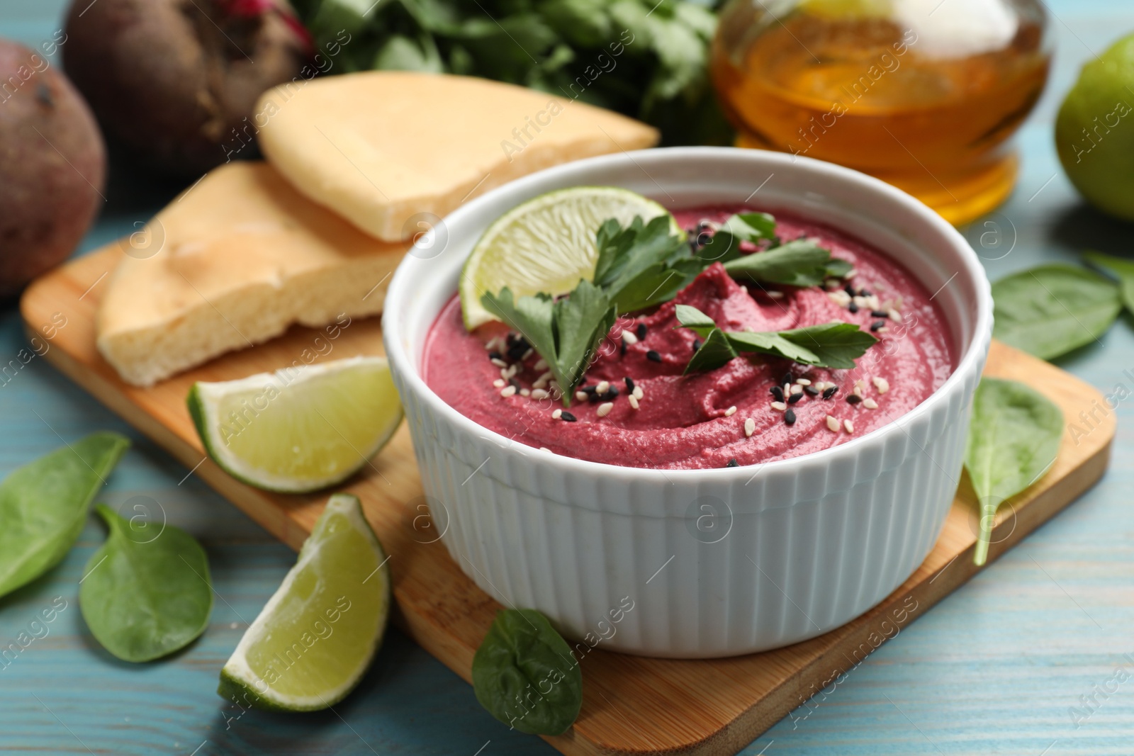 Photo of Tasty beet hummus with parsley and lime in bowl served on light blue wooden table