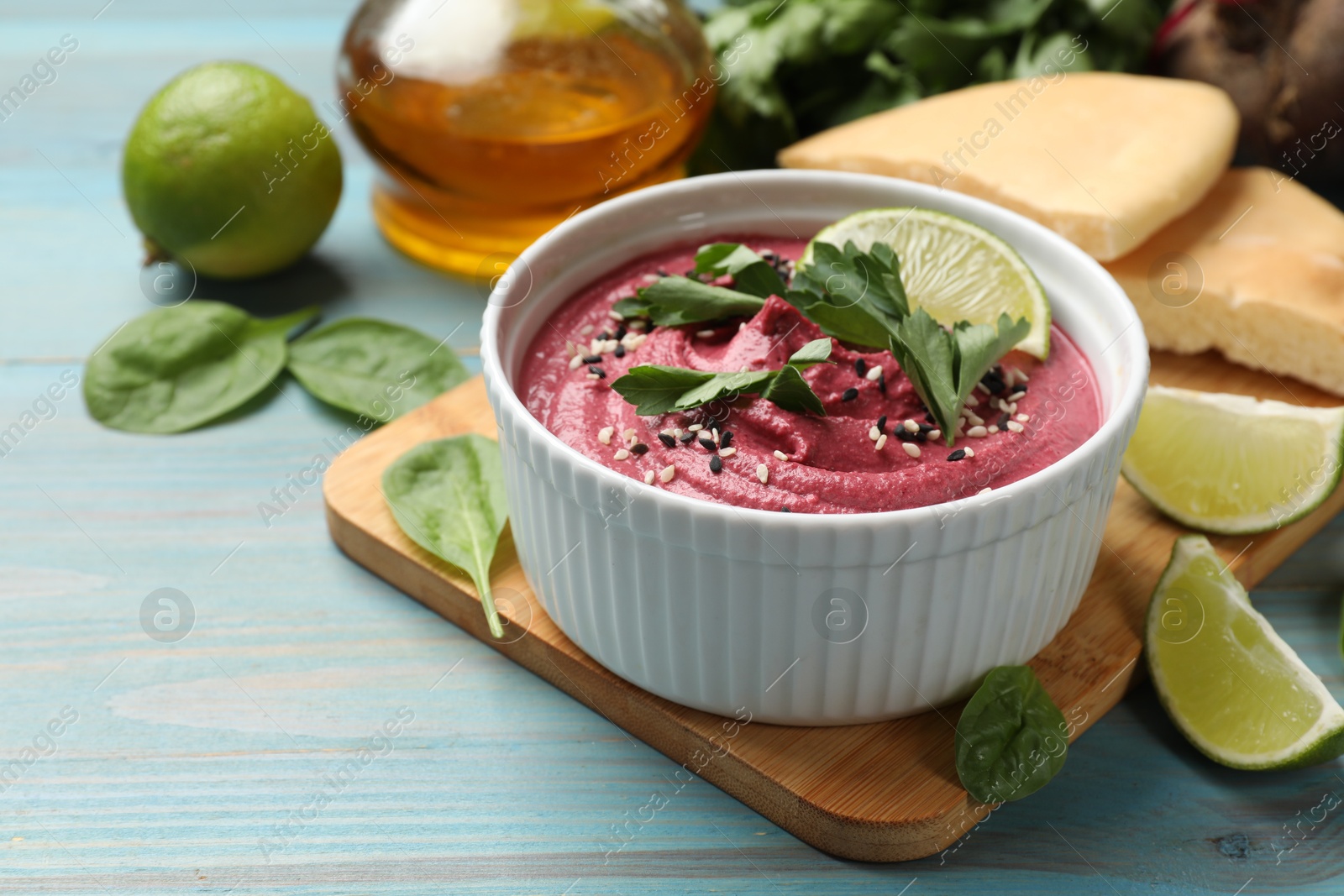 Photo of Tasty beet hummus with parsley and lime in bowl served on light blue wooden table