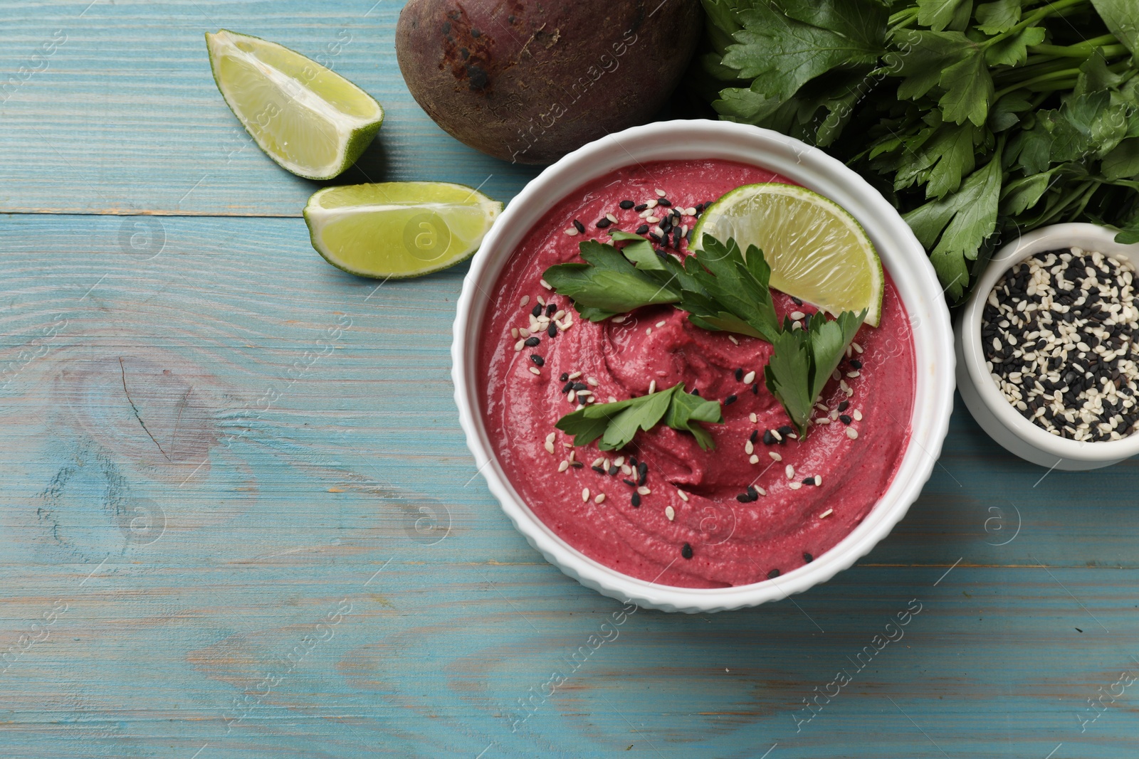 Photo of Tasty beet hummus in bowl and fresh ingredients on light blue wooden table, flat lay. Space for text