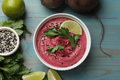 Photo of Tasty beet hummus in bowl and fresh ingredients on light blue wooden table, flat lay