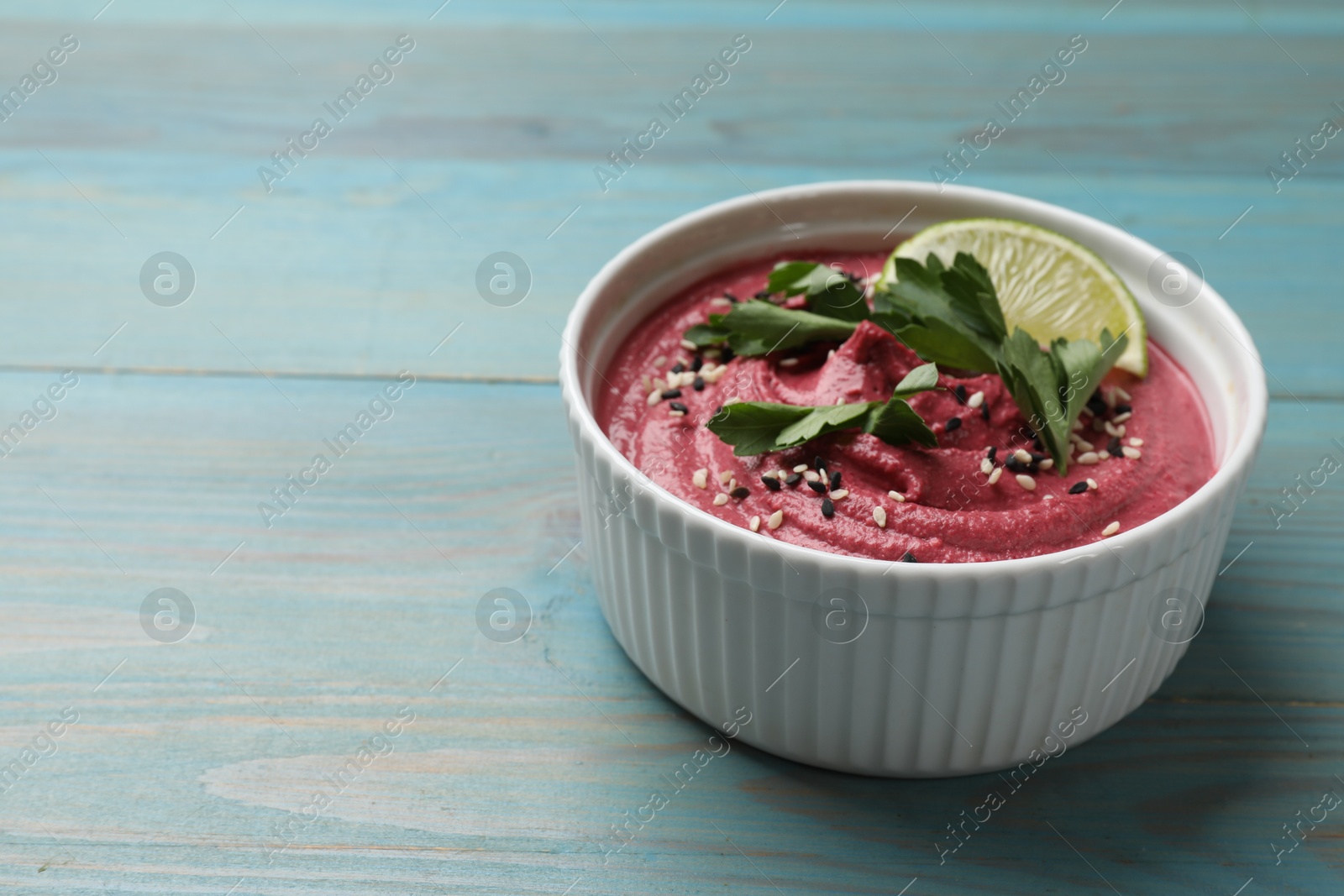 Photo of Tasty beet hummus with parsley and lime in bowl on light blue wooden table. Space for text