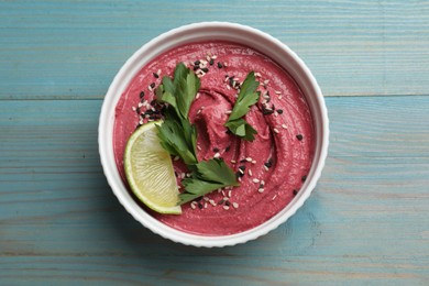 Photo of Tasty beet hummus with parsley and lime in bowl on light blue wooden table, top view