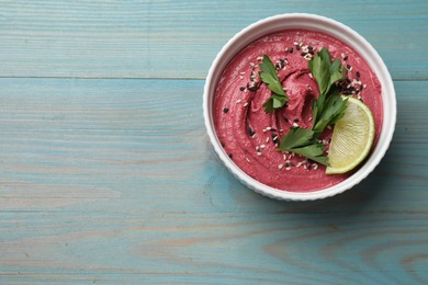 Photo of Tasty beet hummus with parsley and lime in bowl on light blue wooden table, top view. Space for text