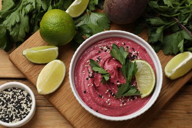 Tasty beet hummus in bowl and fresh ingredients on wooden table, flat lay