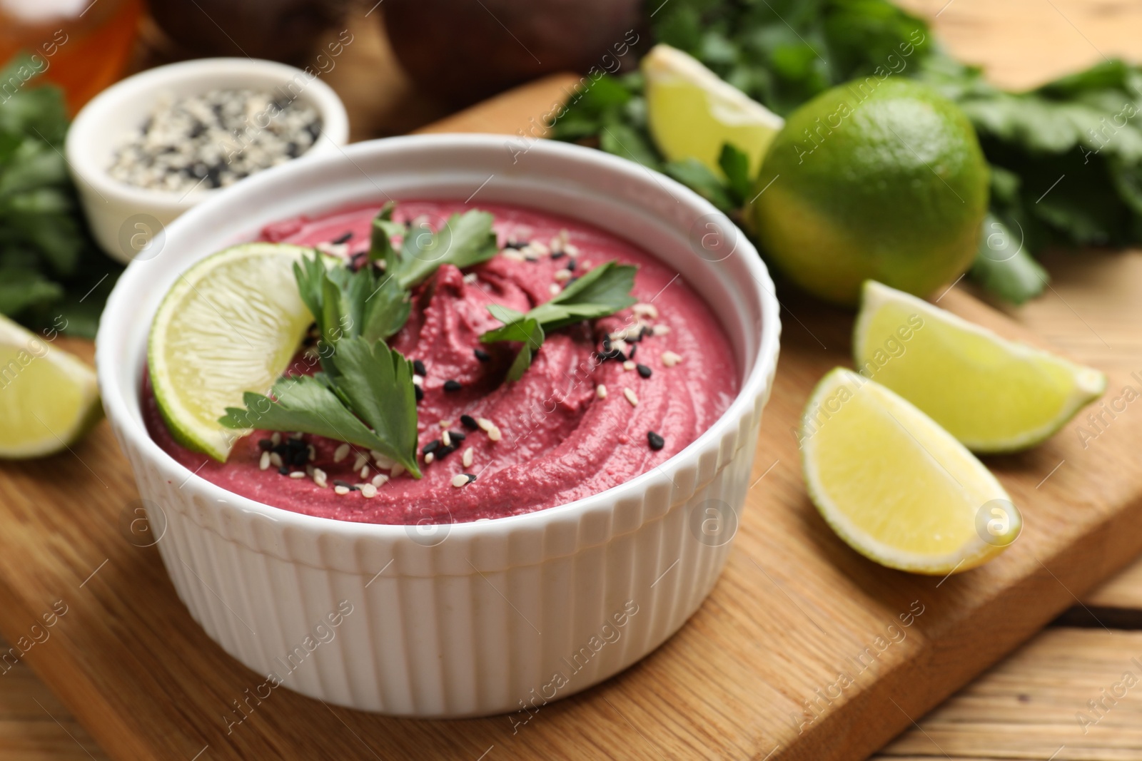 Photo of Tasty beet hummus with lime and parsley in bowl on wooden table, closeup