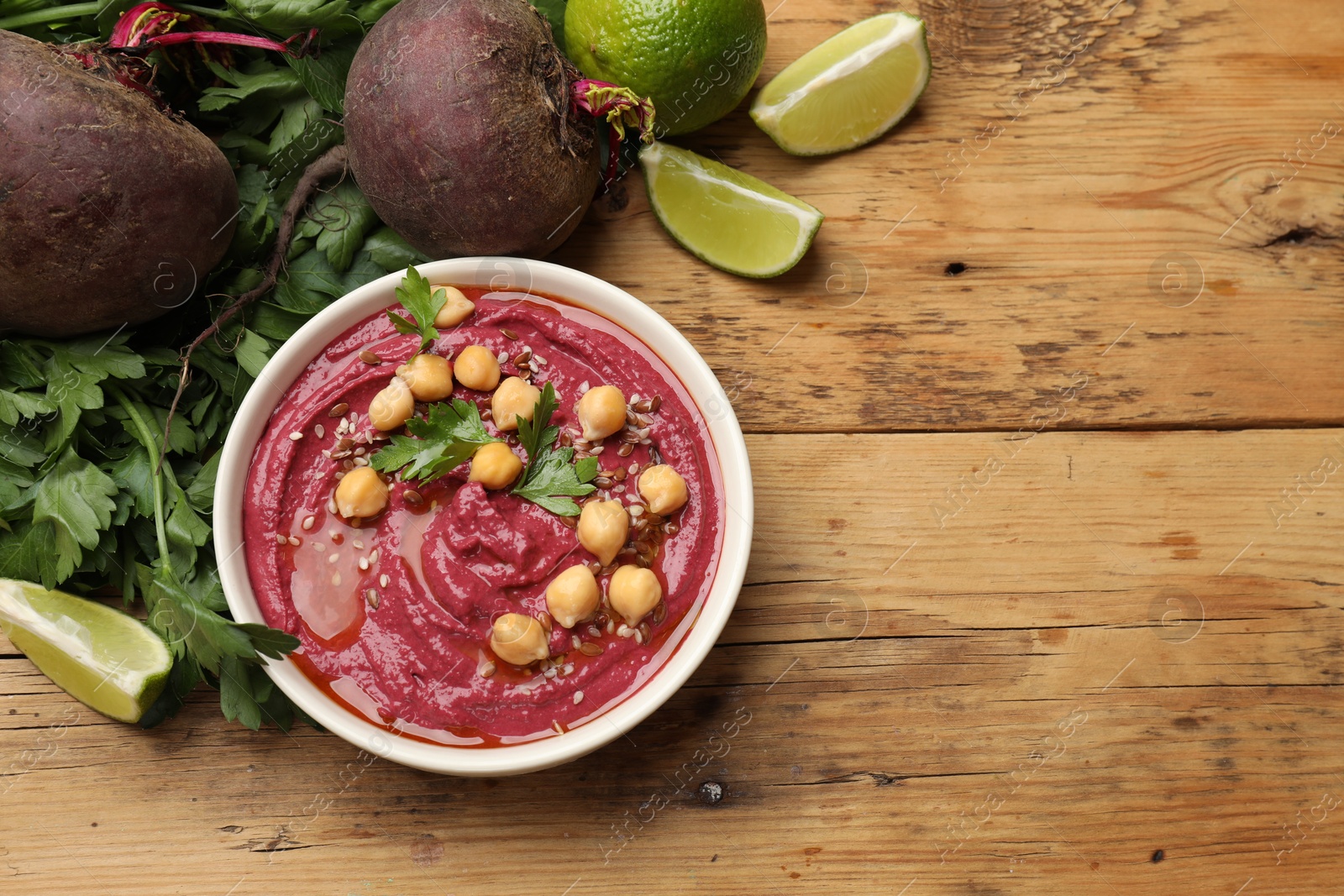 Photo of Tasty beet hummus with chickpeas in bowl and fresh ingredients on wooden table, flat lay. Space for text