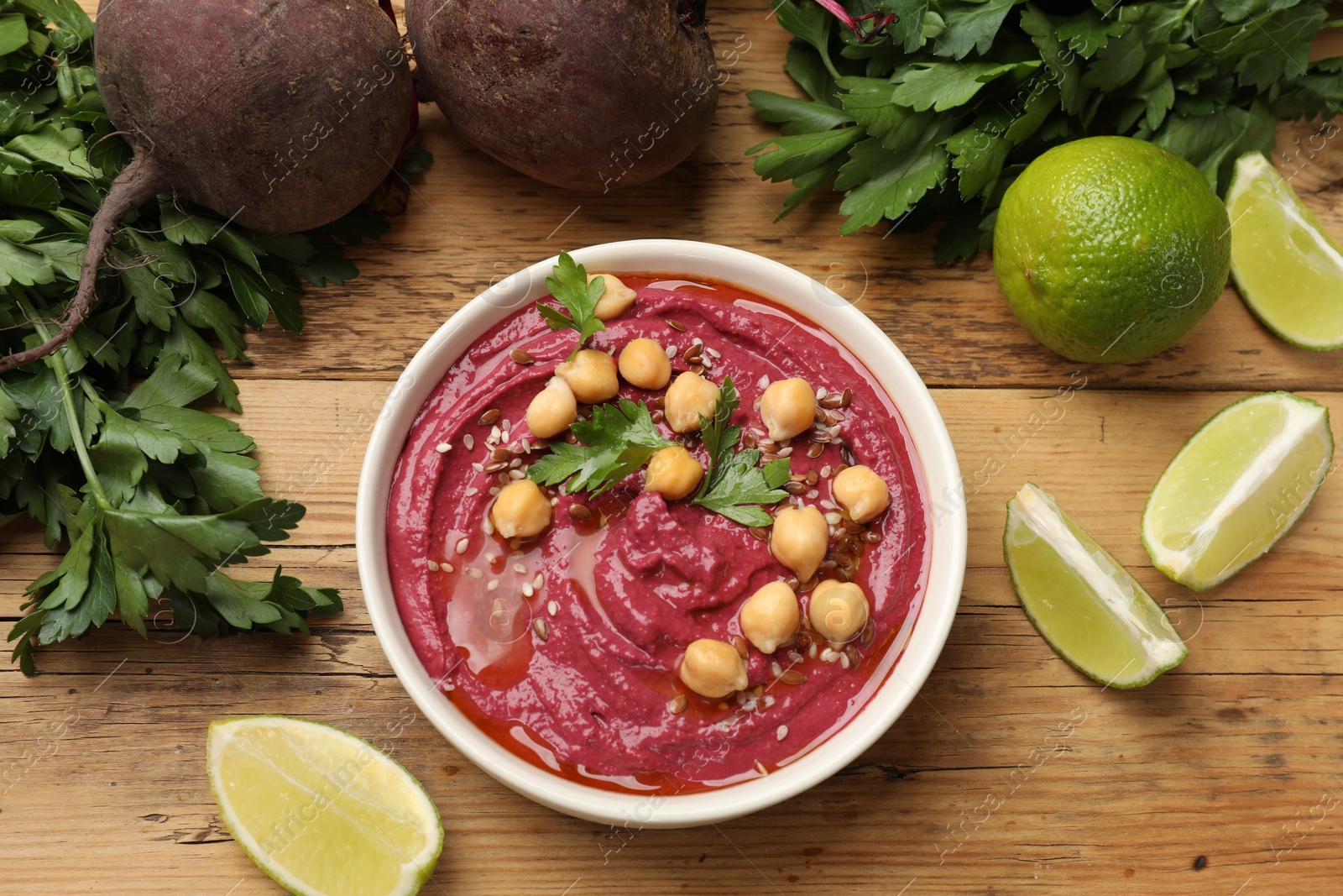 Photo of Tasty beet hummus with chickpeas in bowl and fresh ingredients on wooden table, flat lay