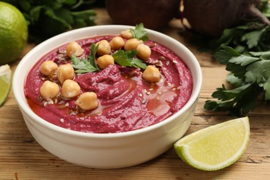 Photo of Tasty beet hummus with chickpeas and parsley in bowl on wooden table, closeup