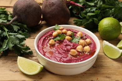 Photo of Tasty beet hummus with chickpeas in bowl and fresh ingredients on wooden table