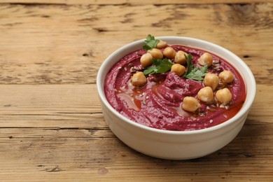 Photo of Tasty beet hummus with chickpeas and parsley in bowl on wooden table. Space for text