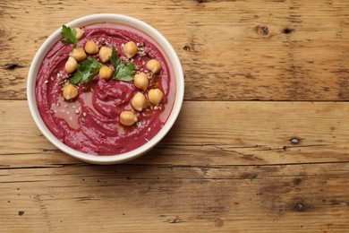 Photo of Tasty beet hummus with chickpeas and parsley in bowl on wooden table, top view. Space for text