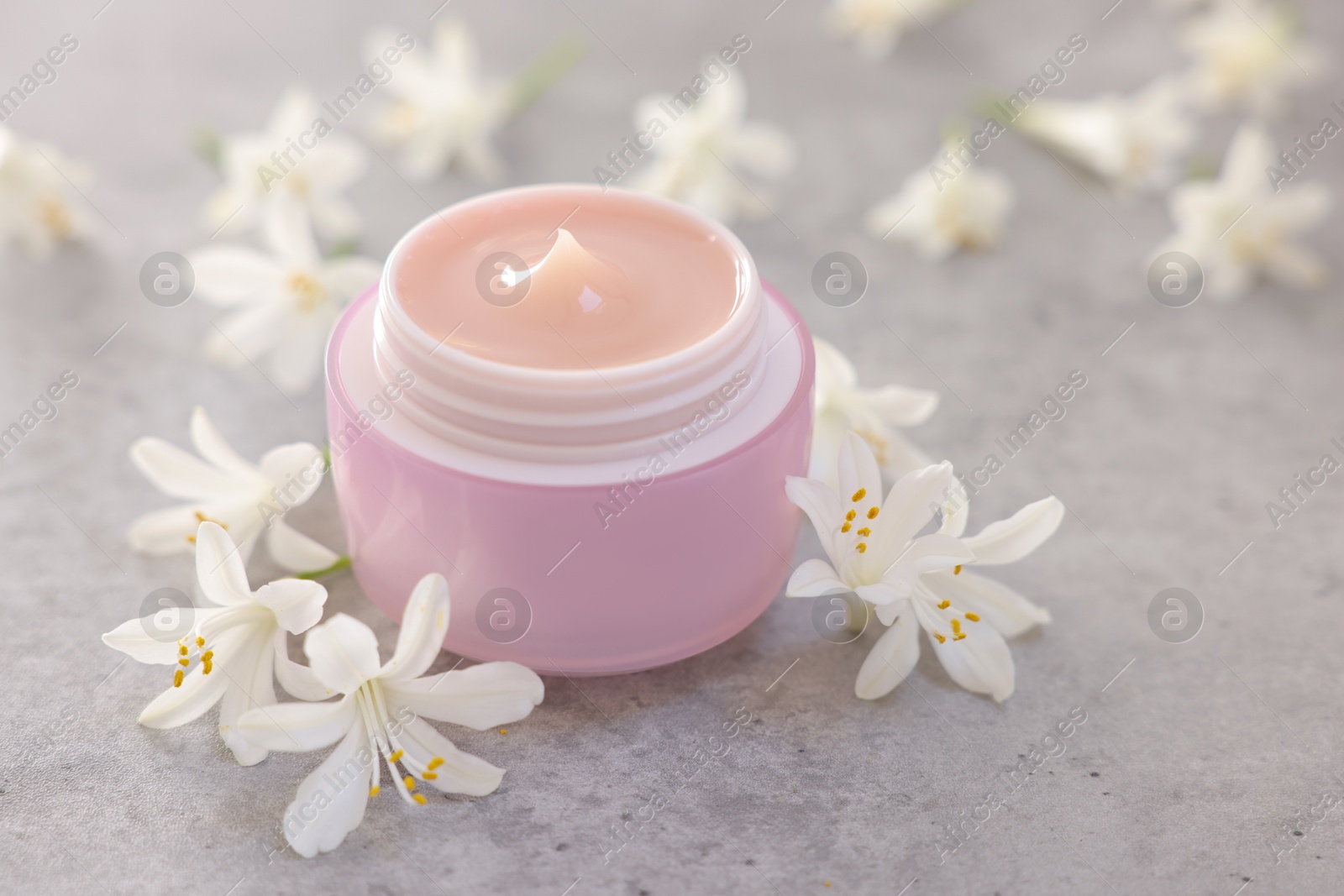 Photo of Cream in jar and jasmine flowers on grey table, closeup