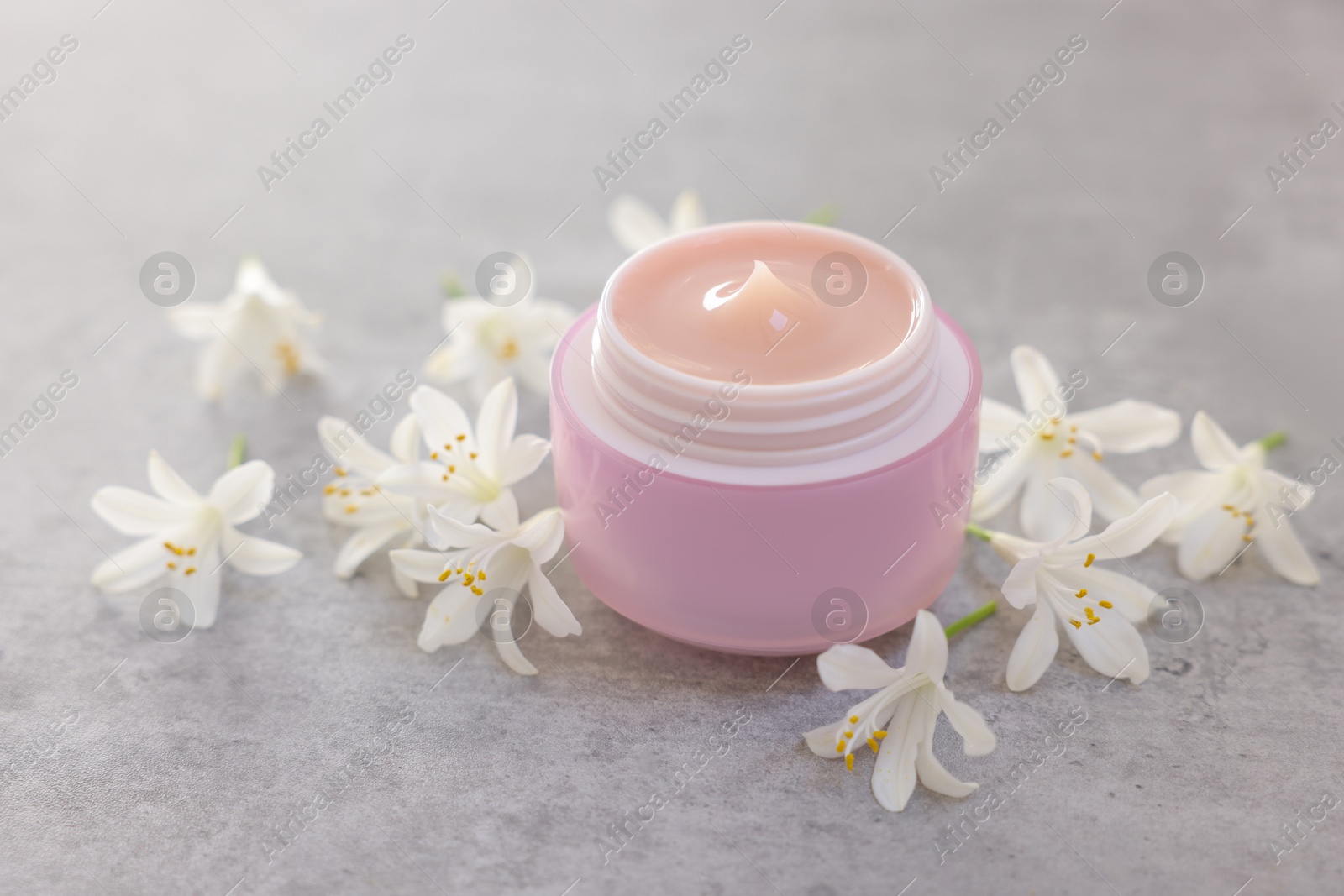 Photo of Cream in jar and beautiful jasmine flowers on grey table, closeup