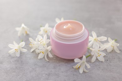 Photo of Cream in jar and beautiful jasmine flowers on grey table, closeup