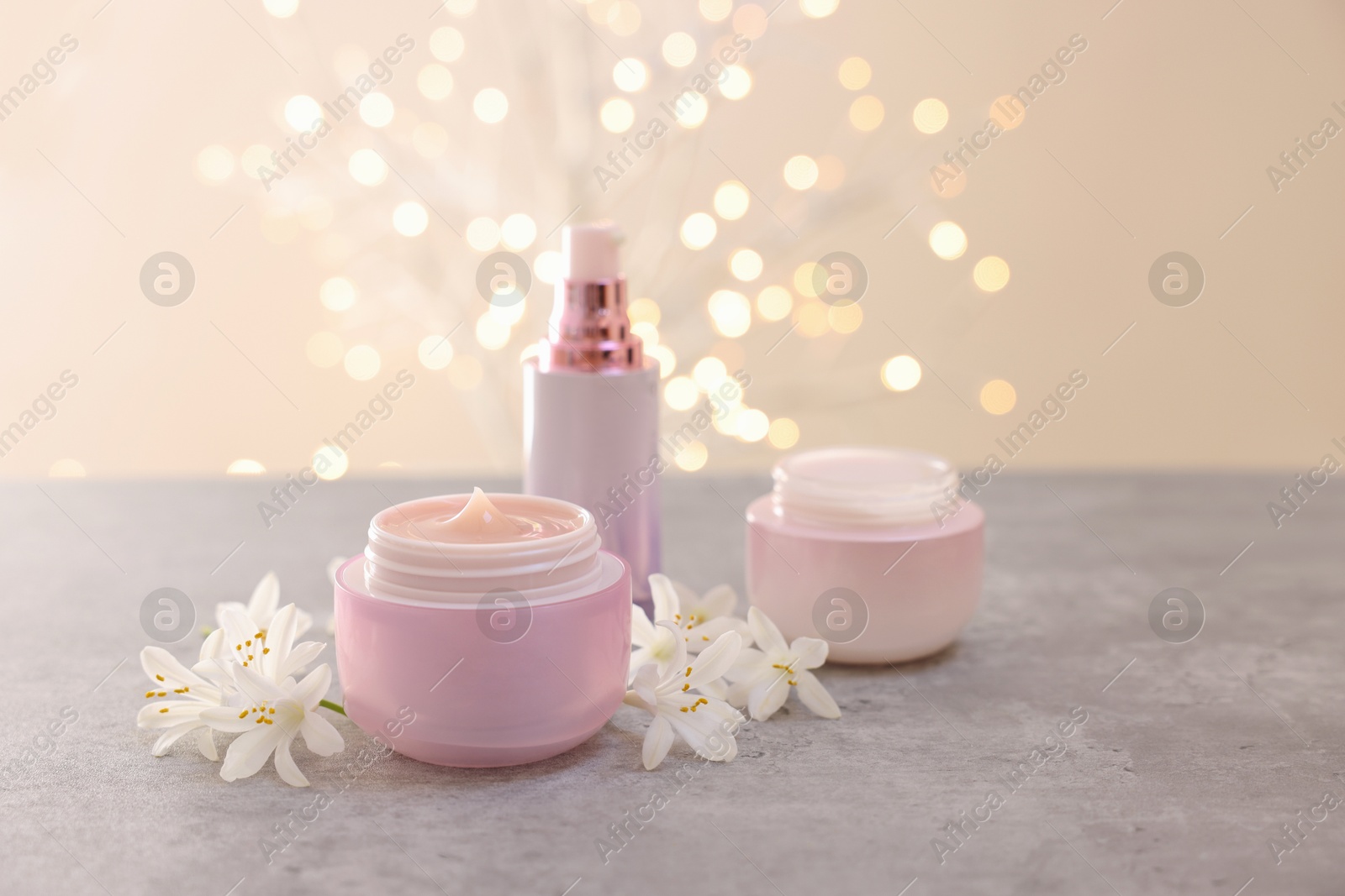 Photo of Cosmetic products and beautiful jasmine flowers on grey table against beige background with blurred lights