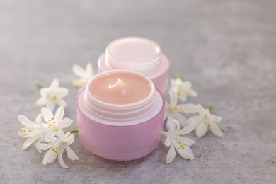 Photo of Cream in jars and beautiful jasmine flowers on grey table, closeup